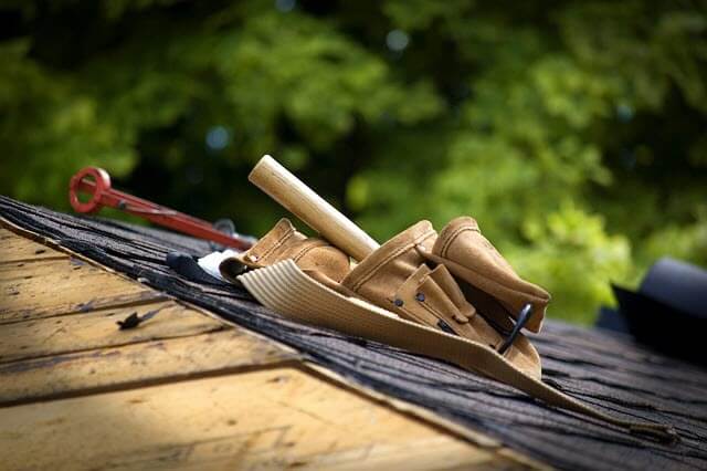 Roofer toolbelt with assorted tools sitting on edge of black shingled roof.